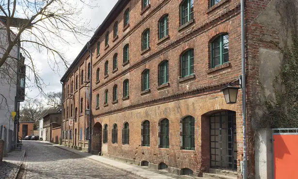 Exterior view of the red brick building of the Stralsund playing card factory on a cobblestone street ©SPEICHER_Leute e.V.